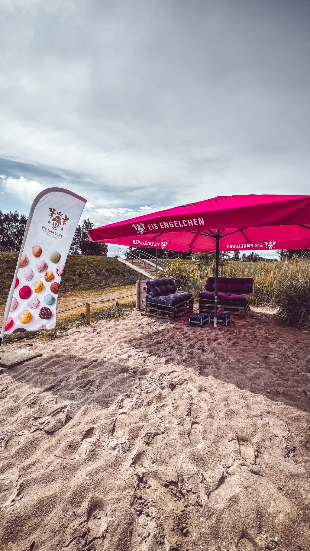 Palettenlounge mit Sonnenschirm im Sand hinterm Deich